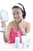 Young woman sitting at dressing table, hand on chin, holding mirror - Asia Images Group