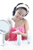 Young woman sitting at dressing table, putting moisturizer on hand - Asia Images Group