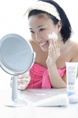 Young woman sitting at dressing table, putting lotion on face - Asia Images Group