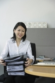 Young woman sitting at office desk, holding stack of binders - Asia Images Group