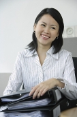 Young woman sitting at office desk, holding binders - Asia Images Group