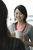 Young woman holding mug, smiling at person in front of her - Asia Images Group