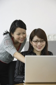 Businesswoman using laptop, another woman looking her shoulder - Asia Images Group