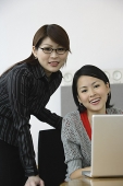 Two businesswomen, smiling at camera, laptop open in front of them - Asia Images Group