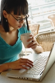 Young woman in cafe, holding cup and using laptop - Asia Images Group