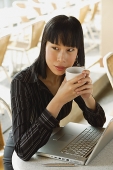 Businesswoman in cafe with laptop, holding cup - Asia Images Group