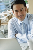 Businessman in cafe with laptop, smiling at camera - Asia Images Group