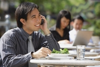 Businessman having lunch at outdoor cafe, using mobile phone - Asia Images Group
