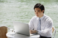 Businessman at outdoor cafe, using laptop, river in the background - Asia Images Group