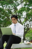 Businessman sitting in park, using laptop - Asia Images Group