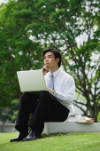 Businessman sitting in park with laptop - Asia Images Group