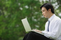 Businessman sitting in park with laptop, side view - Asia Images Group