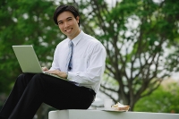 Businessman sitting in park with laptop, looking at camera - Asia Images Group