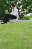 Businessman sitting in park using laptop - Asia Images Group