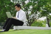 Young businessman sitting in park using laptop - Asia Images Group