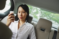 Businesswoman in backseat of car using mobile phone, text messaging - Asia Images Group