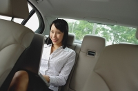 Businesswoman in backseat of car using laptop, smiling - Asia Images Group