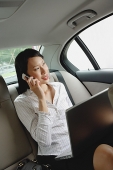 Businesswoman in car using laptop and mobile phone - Asia Images Group