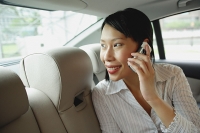 Businesswoman in backseat of car using mobile phone, smiling - Asia Images Group
