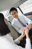 Two businesspeople in backseat of car, exchanging business cards - Asia Images Group