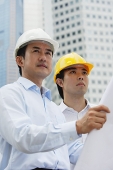 Men in hardhats, holding blueprints, buildings in the background - Asia Images Group