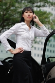 Businesswoman using mobile phone, hand on hip, leaning on car door - Asia Images Group