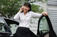 Businesswoman using mobile phone, leaning on car door - Asia Images Group