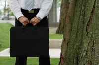 Businessman standing in park, holding briefcase, cropped image - Asia Images Group