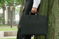 Businessman leaning on tree, holding briefcase, cropped image - Asia Images Group