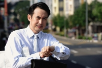 Businessman looking at watch, frowning - Asia Images Group