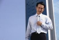 Businessman standing looking at camera, hand on tie - Asia Images Group