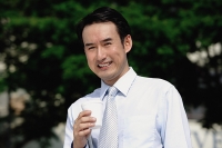 Businessman holding disposable cup, smiling at camera - Asia Images Group
