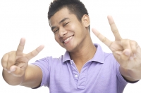 Man smiling, making peace hand sign - Asia Images Group