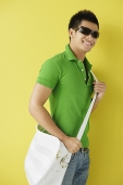 Man in green polo shirt, standing against yellow background, sunglasses on - Asia Images Group