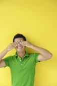 Man standing against yellow wall, covering eyes - Asia Images Group