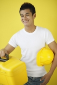 Man carrying construction hat and toolbox, smiling at camera - Asia Images Group