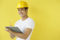 Man wearing hardhat, writing on clipboard, smiling at camera - Asia Images Group