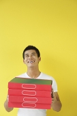 Pizza delivery person carrying a stack of pizza boxes, looking up - Asia Images Group