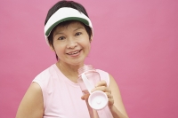 Mature woman wearing sun visor and water bottle, smiling - Asia Images Group