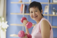 Mature woman using dumbbells, smiling at camera - Asia Images Group