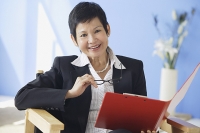 Businesswoman holding clipboard and glasses, smiling at camera - Asia Images Group