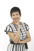 Mature woman against white background, hand on chin, smiling at camera - Asia Images Group