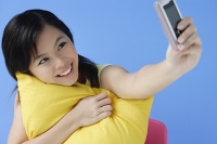 Young woman hugging pillow, using mobile phone to take a picture - Asia Images Group