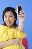 Young woman hugging pillow, using camera phone - Asia Images Group