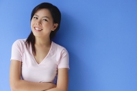 Young woman with arms crossed, standing against blue background - Asia Images Group