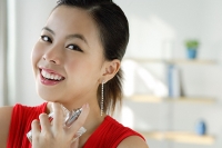 Young woman spraying perfume, smiling at camera - Asia Images Group