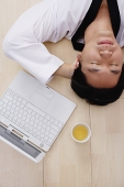 Man lying on floor, hands behind head, laptop next to him - Asia Images Group