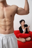 Couple at home, woman sitting on sofa, filing her nails, man in foreground - Asia Images Group