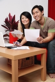 Couple in living room, doing finances, smiling at camera - Asia Images Group