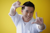 Man making finger frame, smiling at camera - Asia Images Group